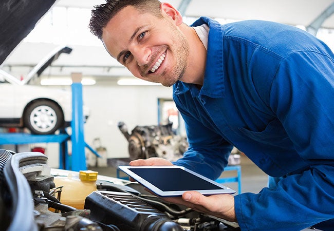 A man stands beside a car, holding a tablet and looking at the screen.