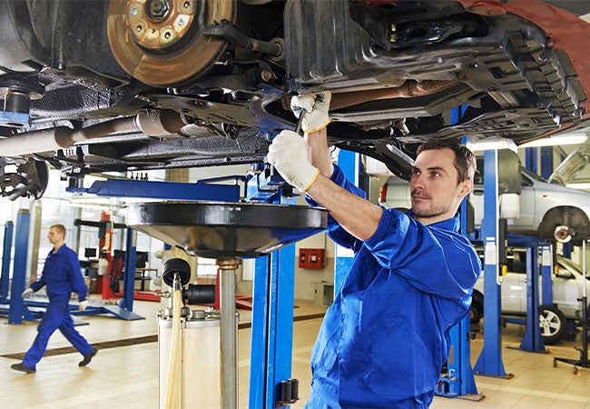 A man in a blue uniform repairs a vehicle in a garage setting.