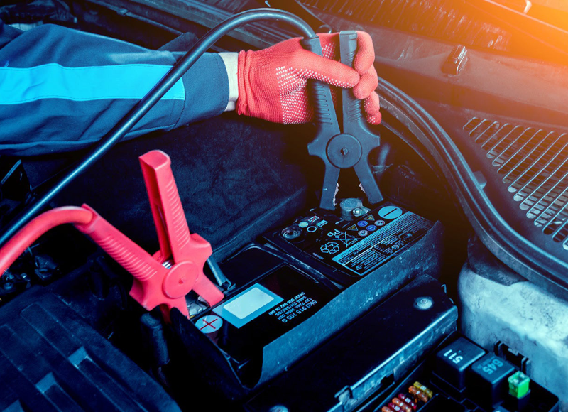 A person connects a jump starter to a car battery, preparing to start the vehicle.